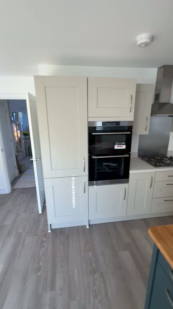 Cream shaker kitchen with built-in ovens, gas hob and blue island with oak worktop
